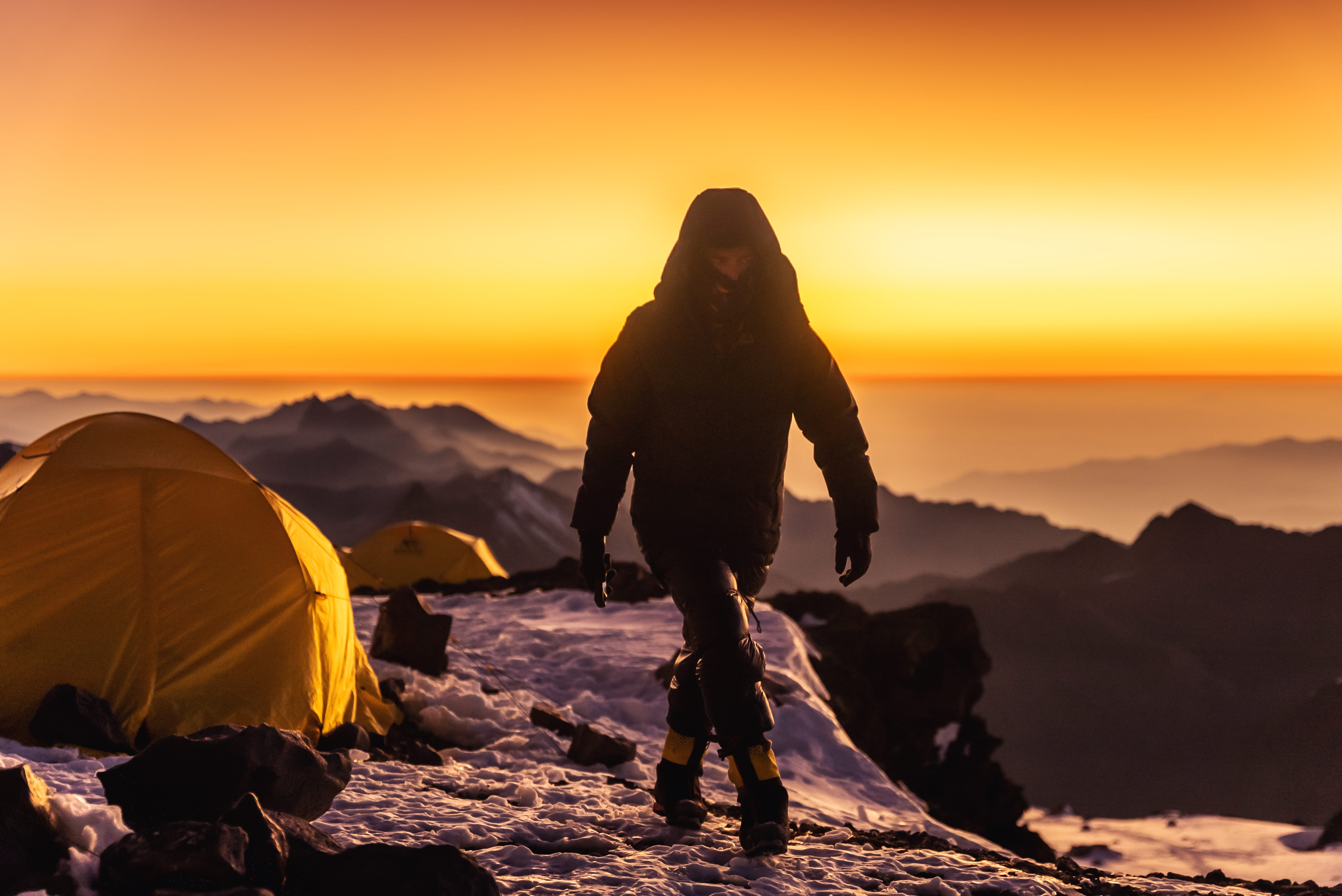 Climber walking past tents at sunrise on the mountain