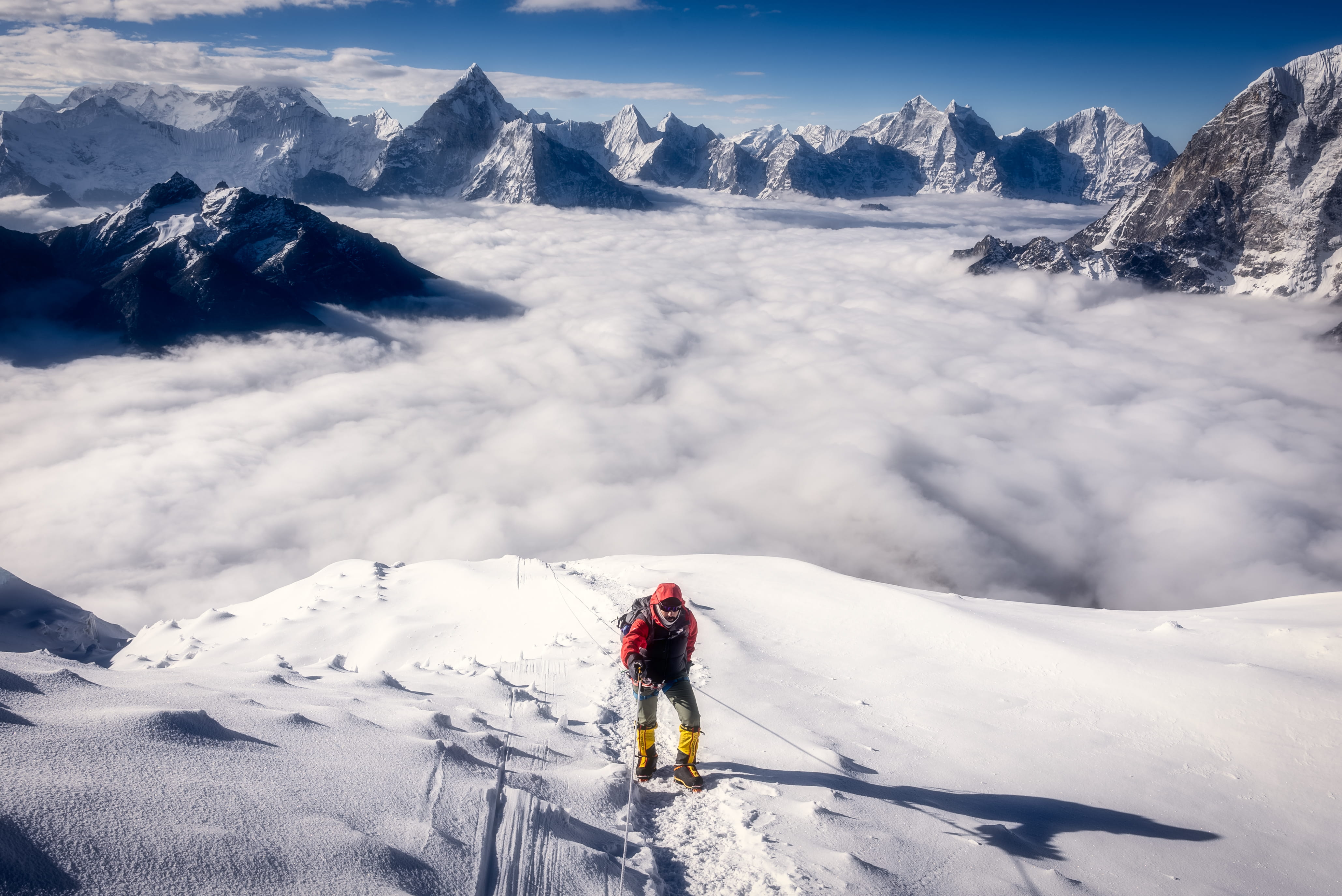 Climber ascending a snow ridge with Himalayan peaks behind